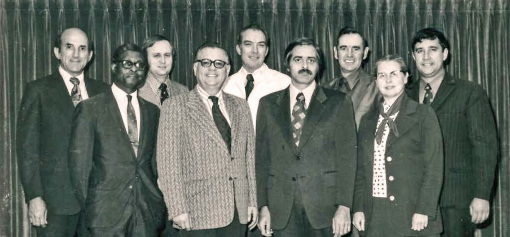 A 1973 photograph of the Mennonite Board of Missions. Back row, left to right: Louis Strite, Robert Summers, Jim Detweiler, James Mullet, Gerald Good. Front: Leamon Sowell, Sam Jantzen, Donald Yoder, Doris Kramer. Photo by Alvin Hostetler.