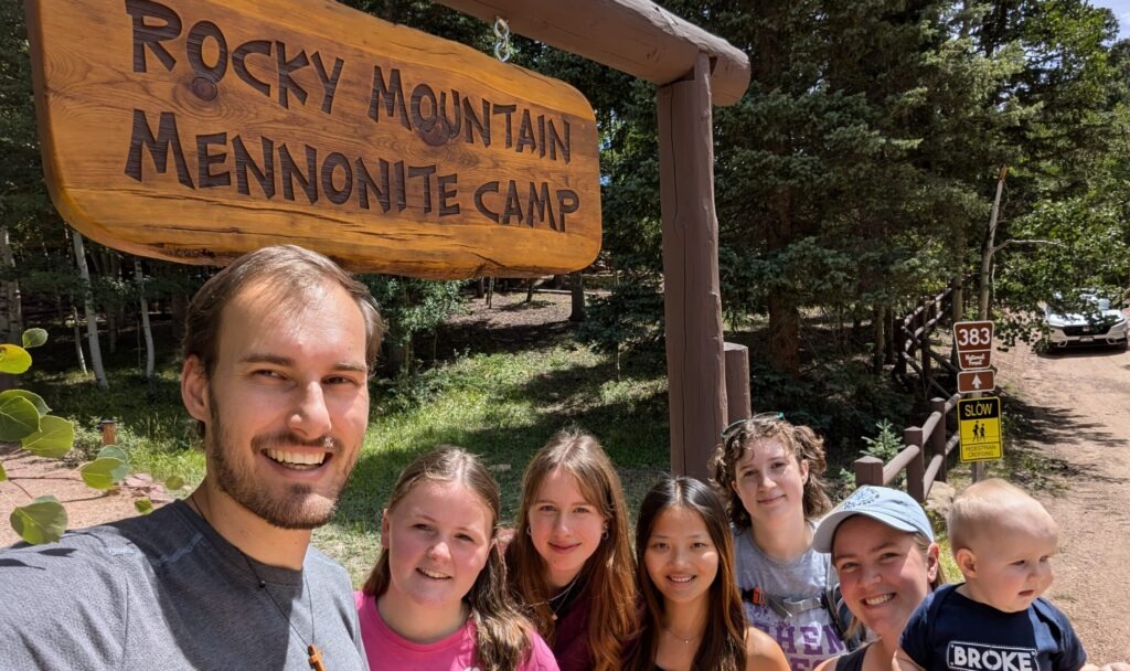 The 2024-25 Colorado Springs unit poses in front of the Rocky Mountain Mennonite Camp entrance sign. The camp is a Mission Network partner and placement site. From left: Christian Stoltzfus (unit leader), Elizabeth Daudey, Alea Sagert, Hannah Smith, Sadie Sherman, Leigha Stoltzfus (unit leader) with daughter Naomi. Photo by Christian Stoltzfus.
