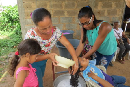 ​Roselyn Rodriguez and Arli Rojas wash Silmarys Rodriguez's hair at Community of Peace Mennonite Church on Isla Margarita. In foreground
