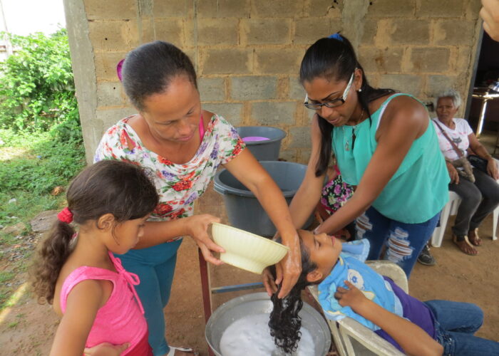 ​Roselyn Rodriguez and Arli Rojas wash Silmarys Rodriguez's hair at Community of Peace Mennonite Church on Isla Margarita. In foreground