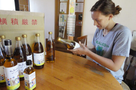 Tierney Frey attaches labels to the bottles of canola oil produced by Menno Village during Youth Venture Japan this summer. Photo by Abby Findley. Download full resolution image.