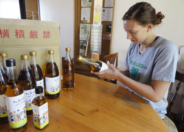 Tierney Frey attaches labels to the bottles of canola oil produced by Menno Village during Youth Venture Japan this summer. Photo by Abby Findley. Download full resolution image.